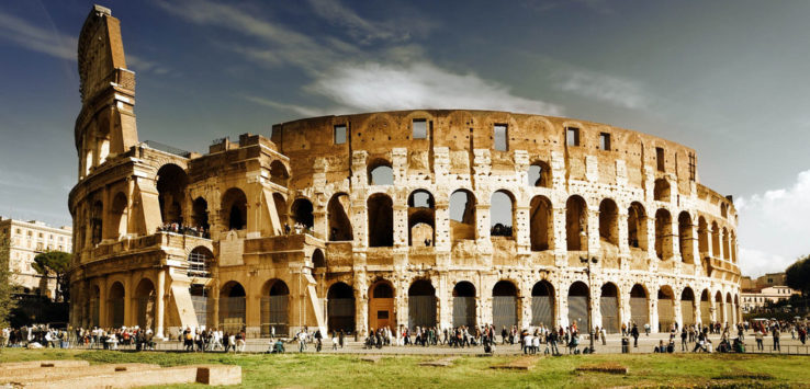 a large circular stone building with many arches with Colosseum in the background