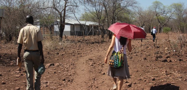 a man and woman walking on a dirt path with a red umbrella