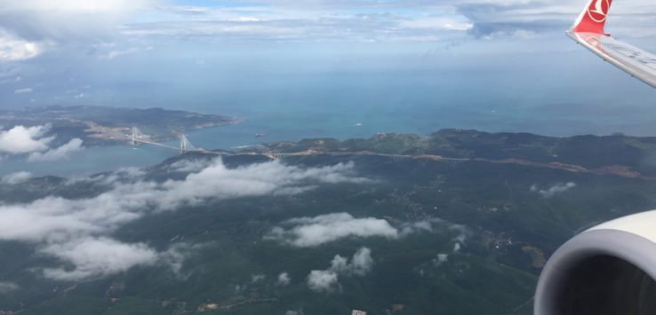 an aerial view of a landscape with clouds and a bridge