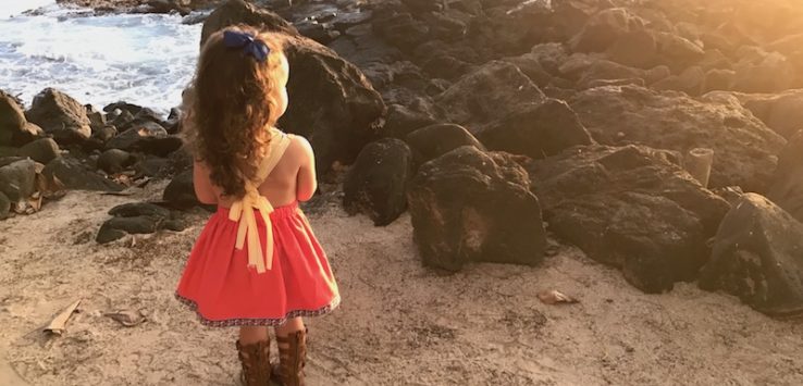 a girl standing on a rocky beach looking at the ocean