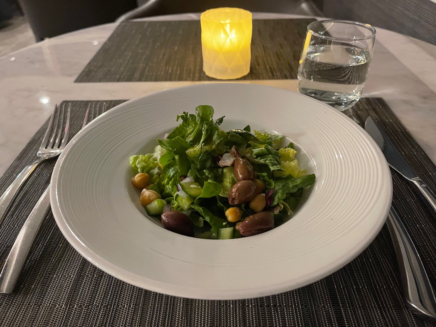 a plate of salad with a candle and a glass of water