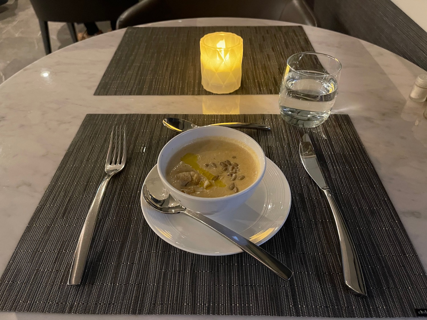 a bowl of soup on a plate with spoons and fork and knife