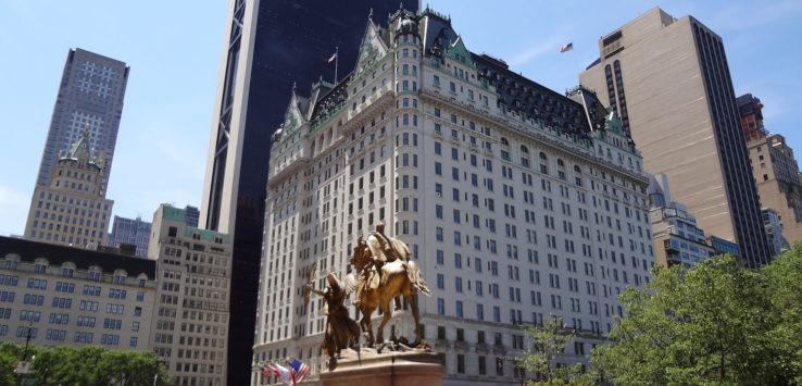 a statue of a man on a horse in front of a large building with Plaza Hotel in the background
