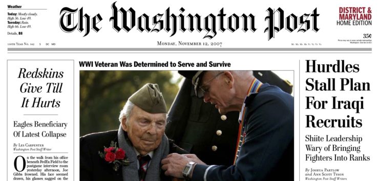 a man in military uniform putting on a man's jacket