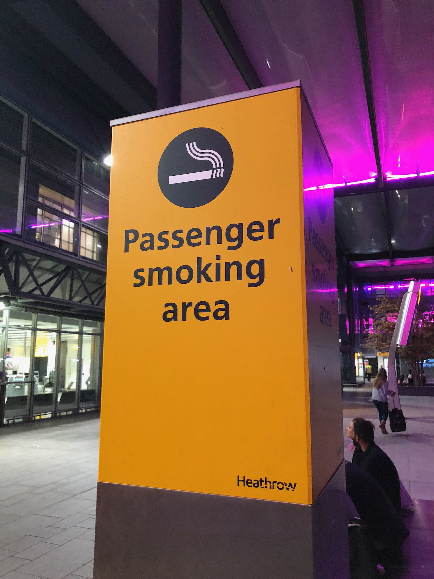 a yellow sign with black text and a man sitting in front of a building