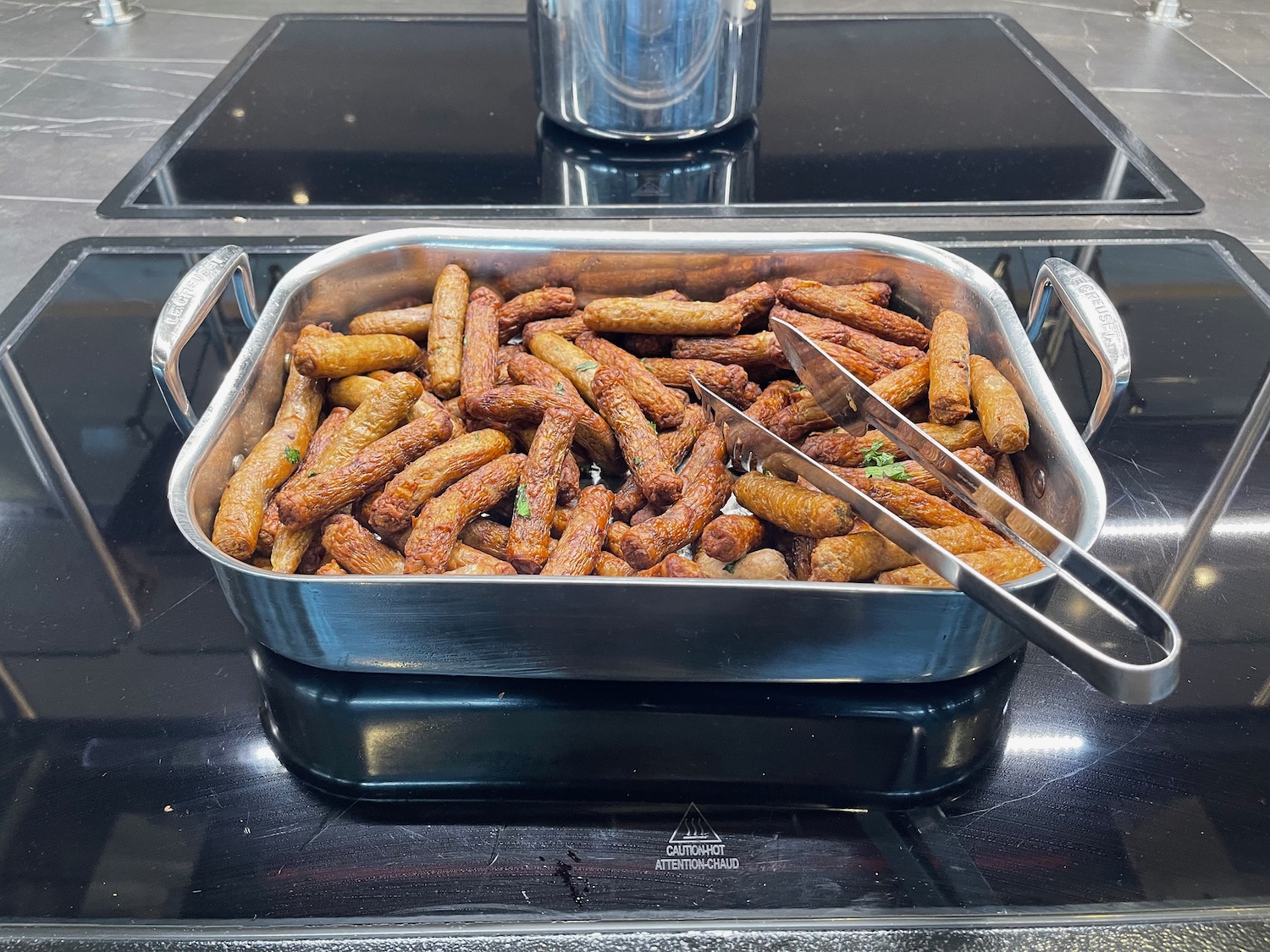 a pan of sausages and tongs