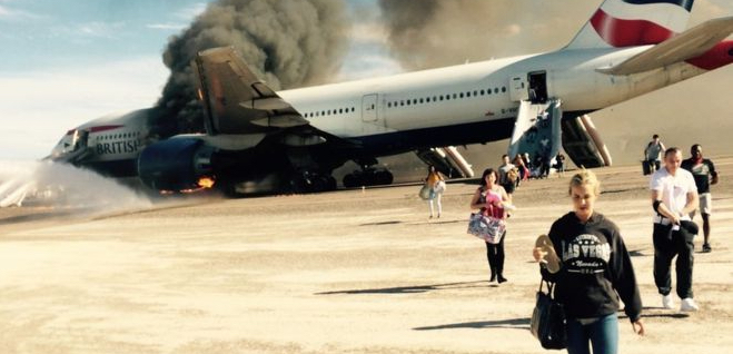a group of people walking on a runway with a plane on fire
