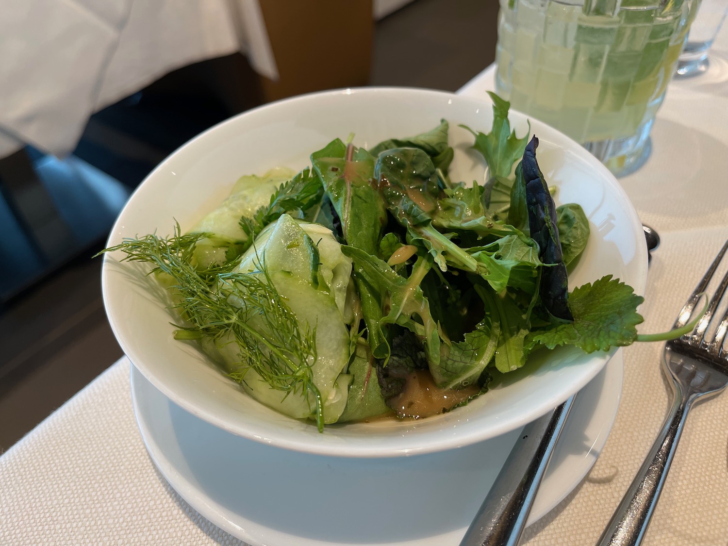 a bowl of salad with greens and a glass of water