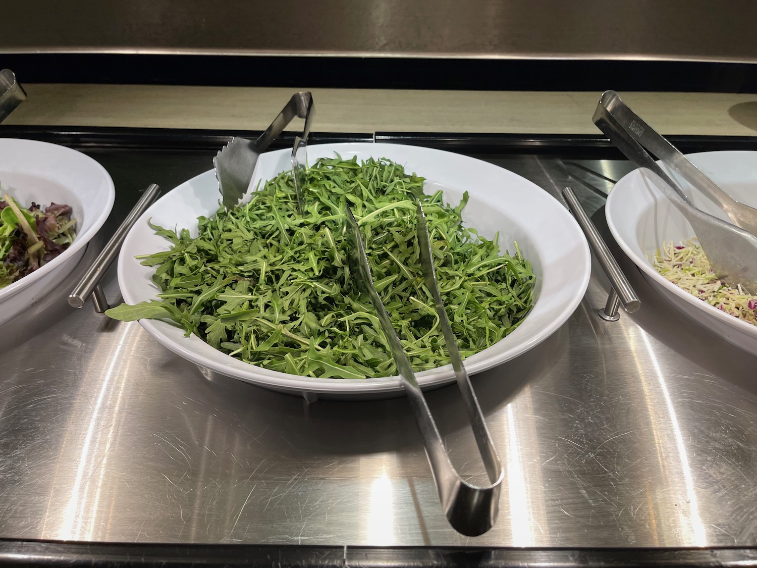 a bowl of greens with tongs