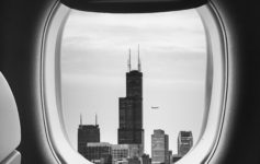 a window of an airplane with a tall building in the distance