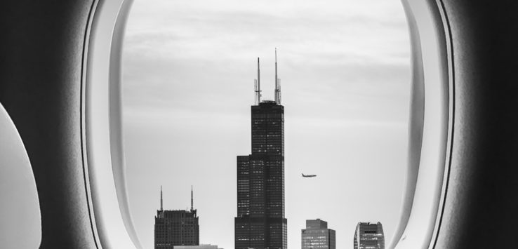 a window of an airplane with a tall building in the distance