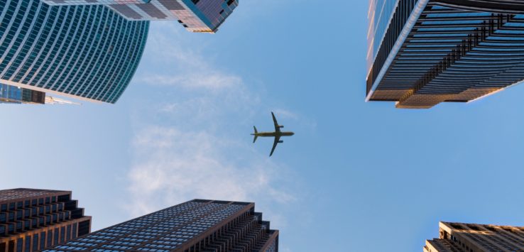 a plane flying in the sky over tall buildings