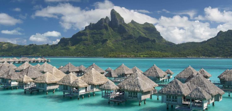 a group of huts in water with Bora Bora in the background