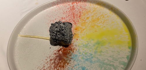 a black and yellow toothpick on a white plate with rainbow colors