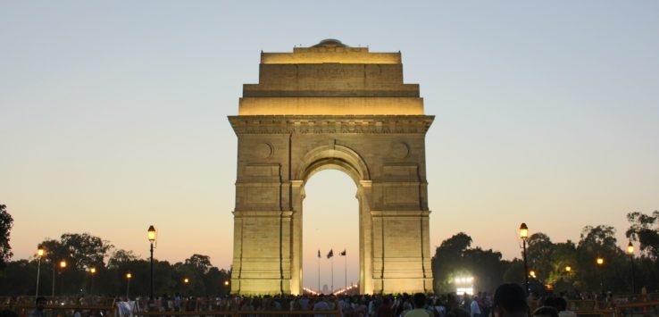 a large stone arch with people walking around with India Gate in the background