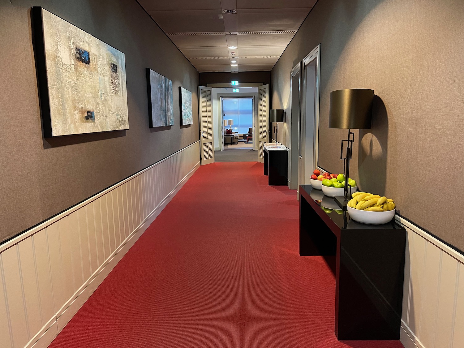 a hallway with a red carpet and a table with fruit on it
