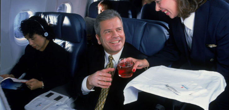 a man sitting in an airplane with a woman holding a drink
