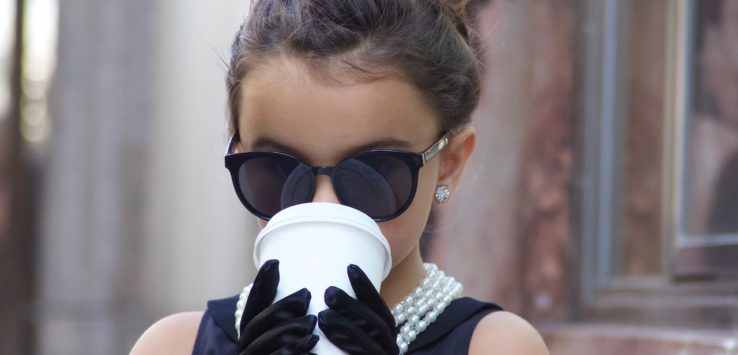 a girl wearing sunglasses and a necklace and holding a cup