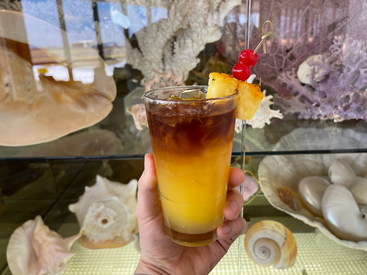 a hand holding a glass of liquid with a cherry and pineapple