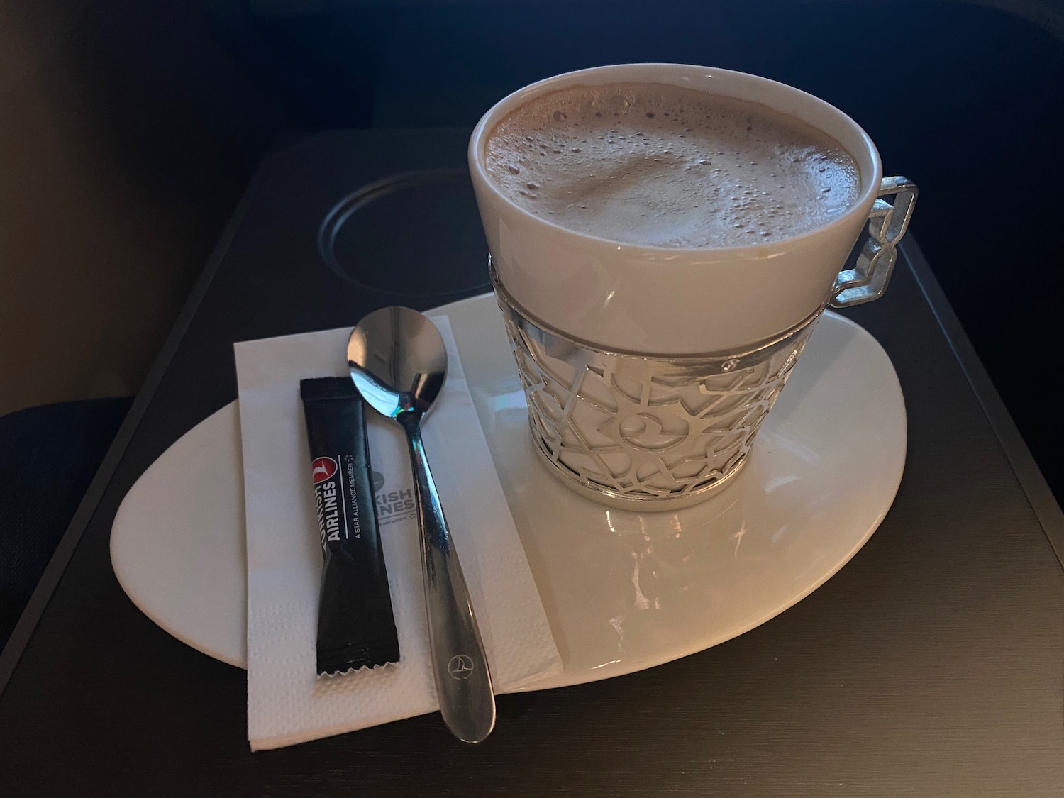 a cup of coffee on a plate with a spoon and sugar packet