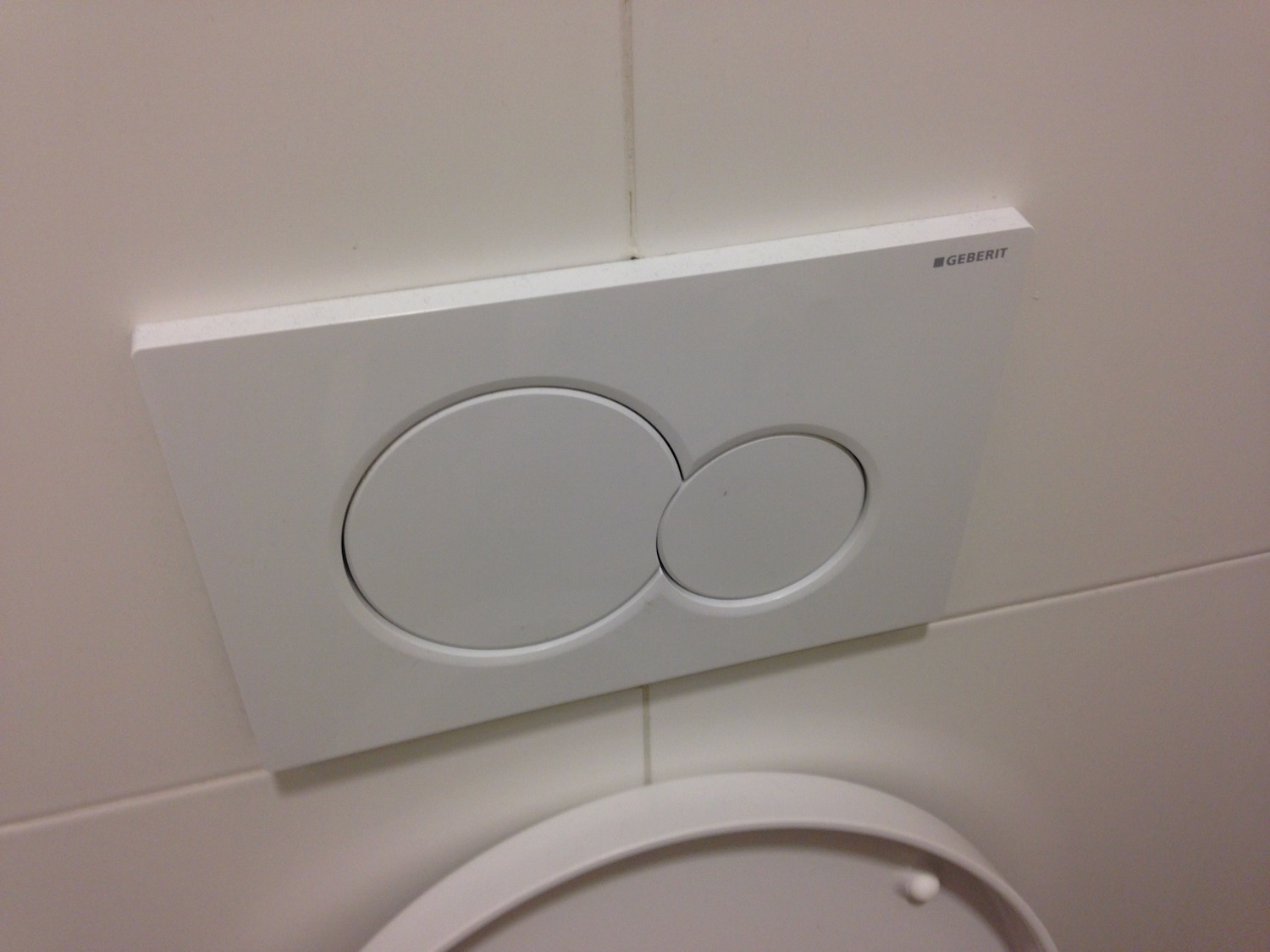 a white toilet with two circular buttons
