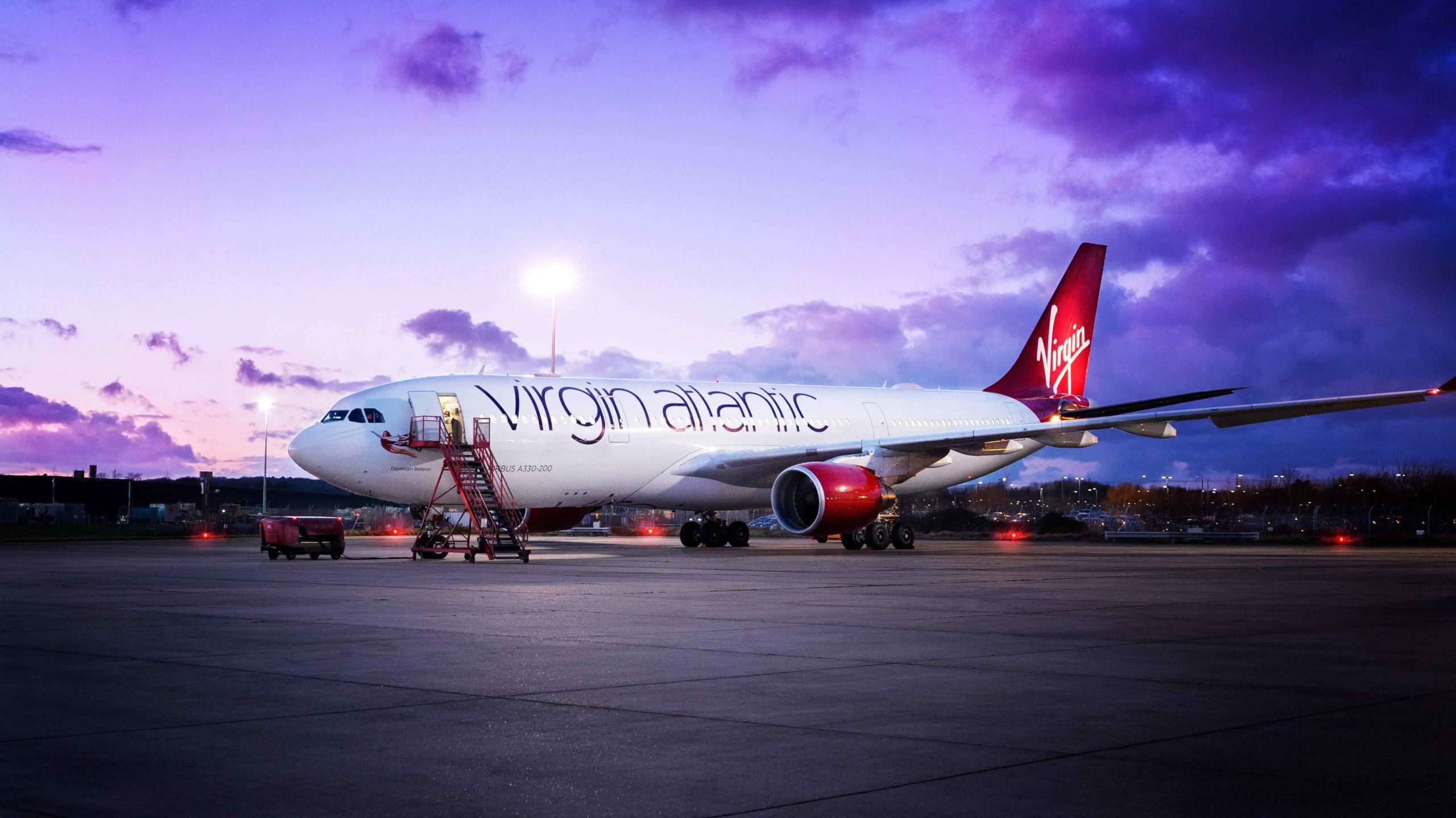 a large white airplane with red tail and a ladder on the ground