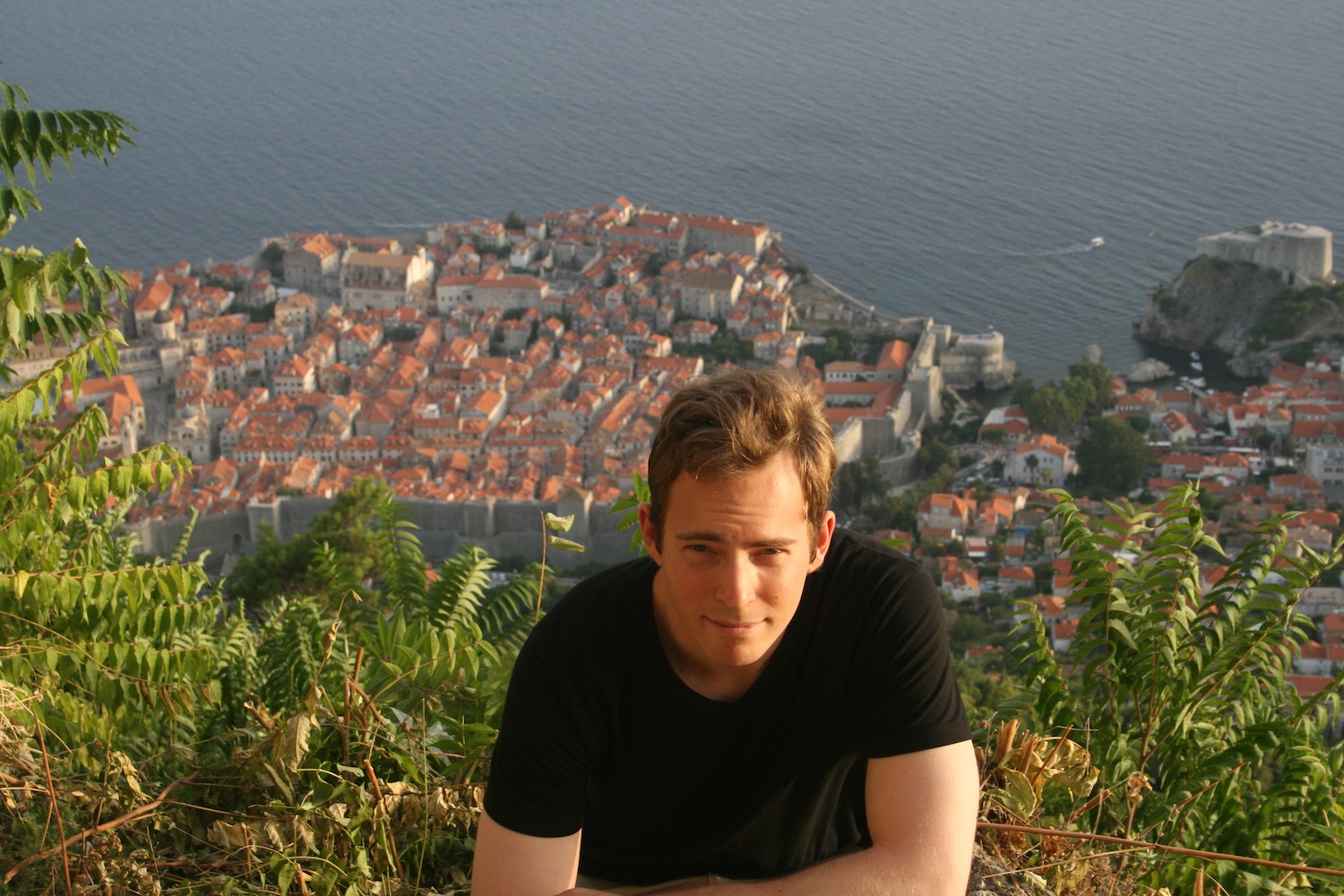 a man sitting on a hill with a city in the background