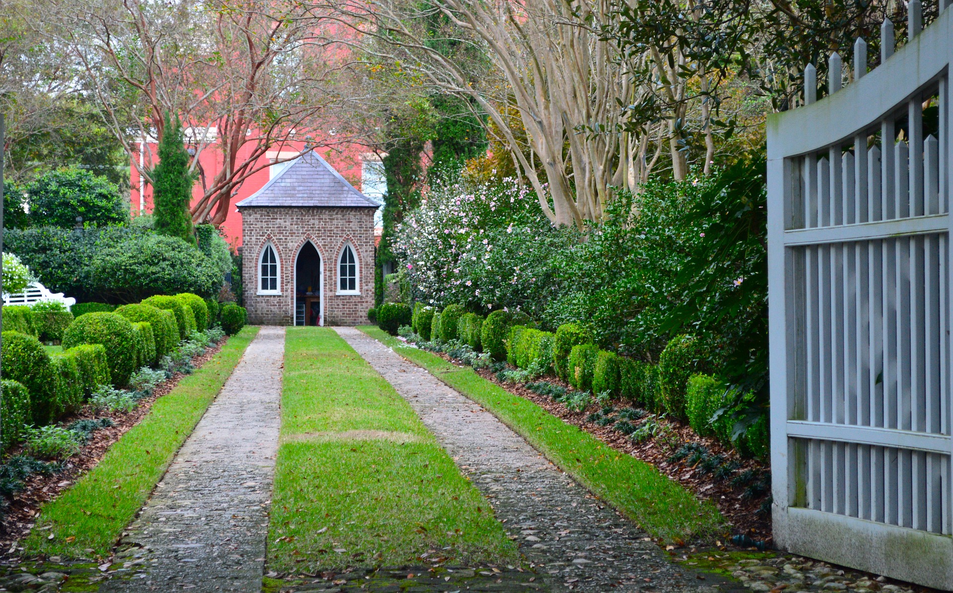 a brick building with a small chapel and a path with bushes and trees