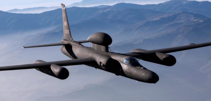 a black airplane flying over mountains