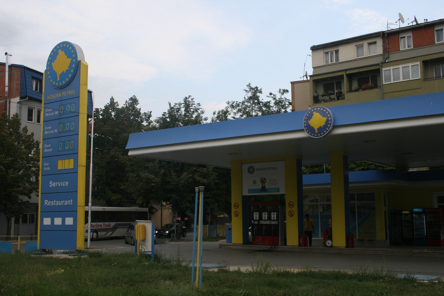 a gas station with a sign and a bus in the background