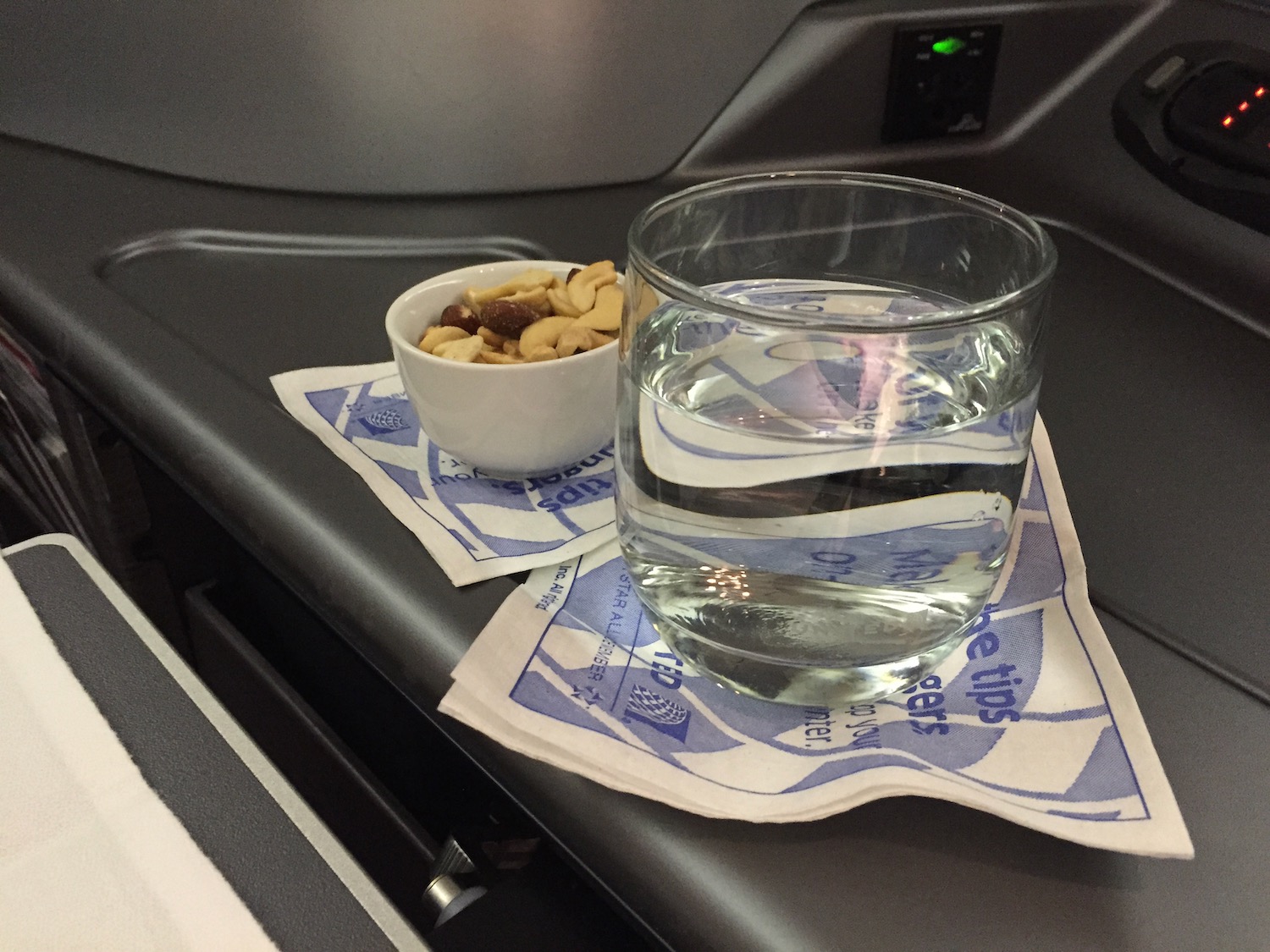 a glass of water and a bowl of nuts on a napkin