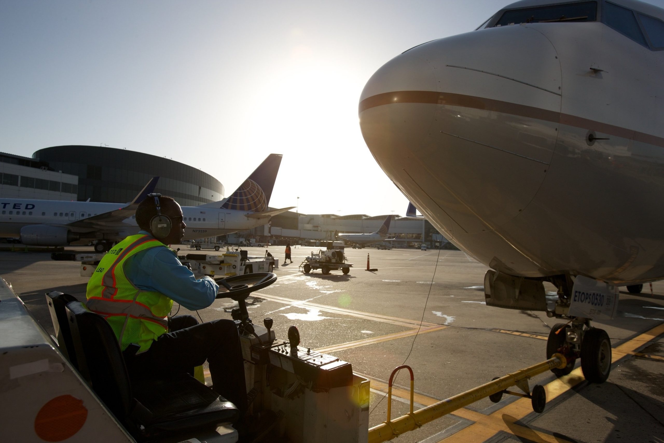 a man in a yellow vest and headphones sitting in front of a plane