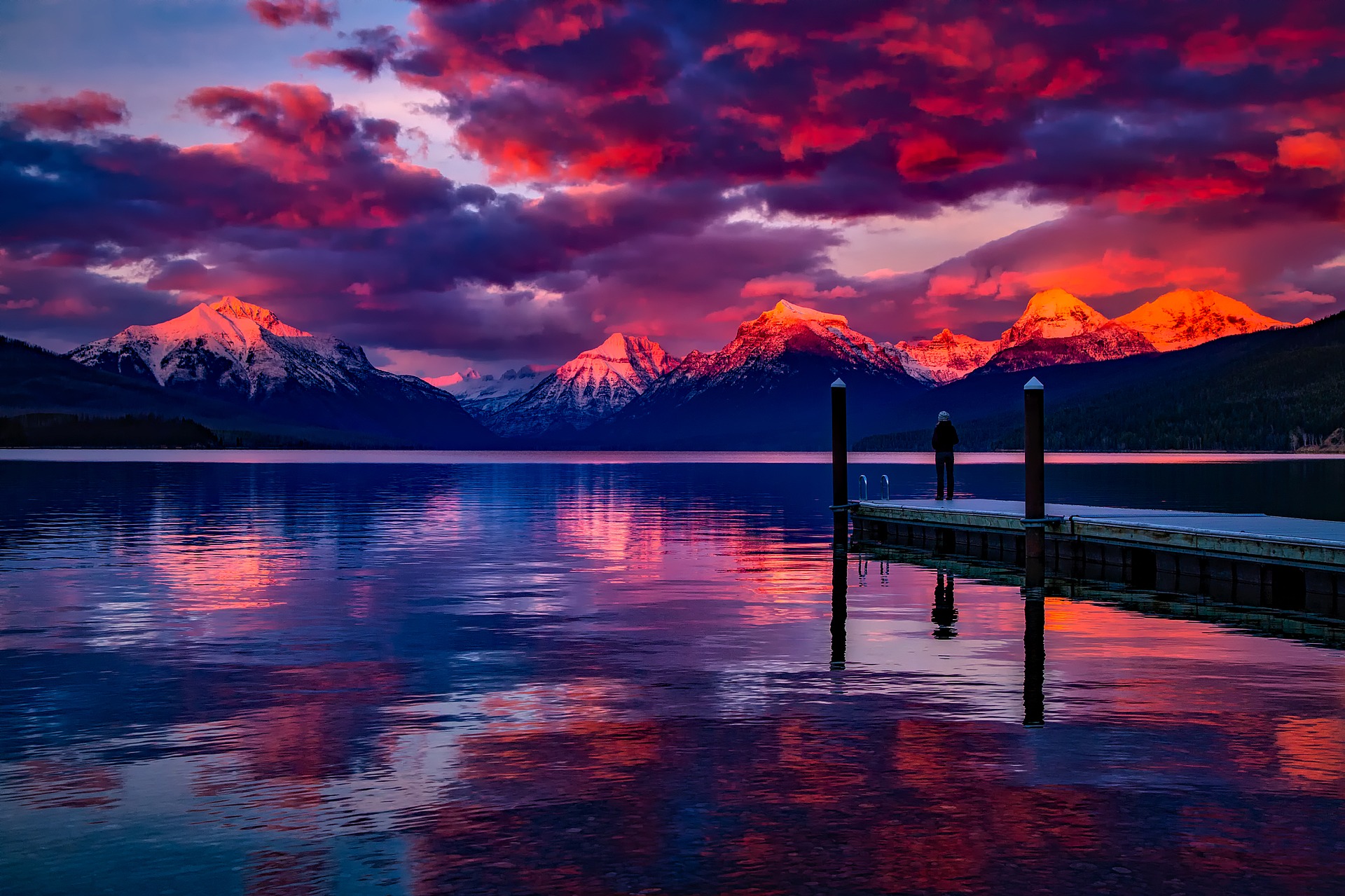 a person standing on a dock on a lake with mountains in the background