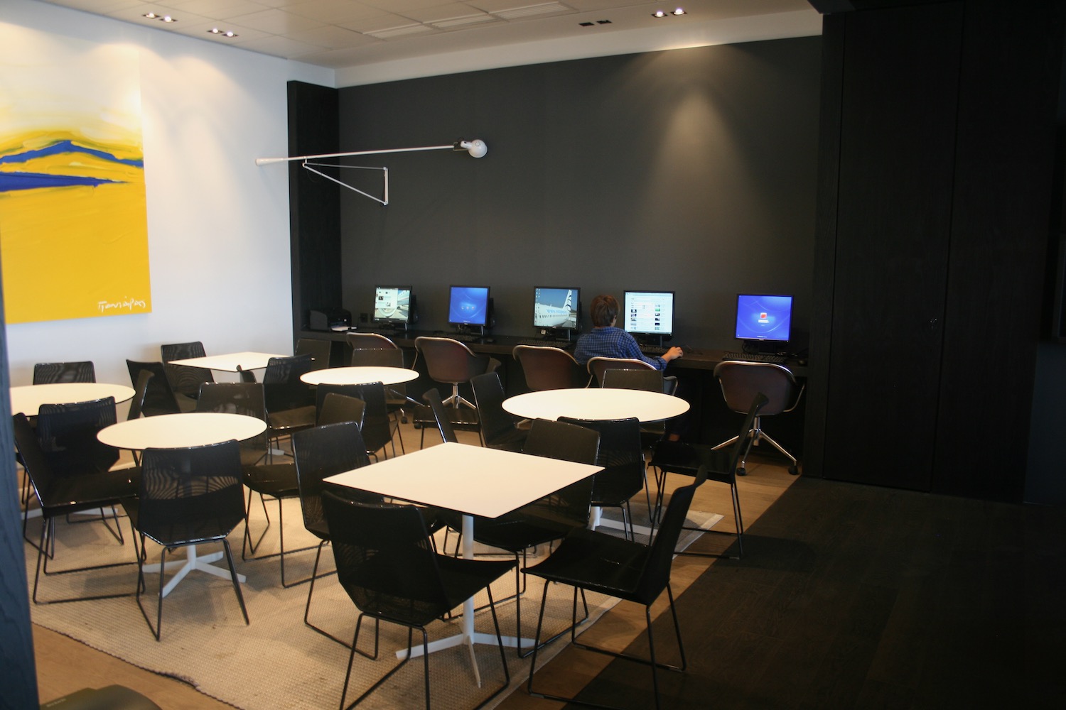 a room with many tables and chairs and a man using computers