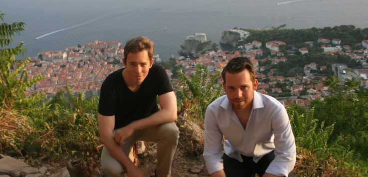 two men sitting on a hill with a city in the background