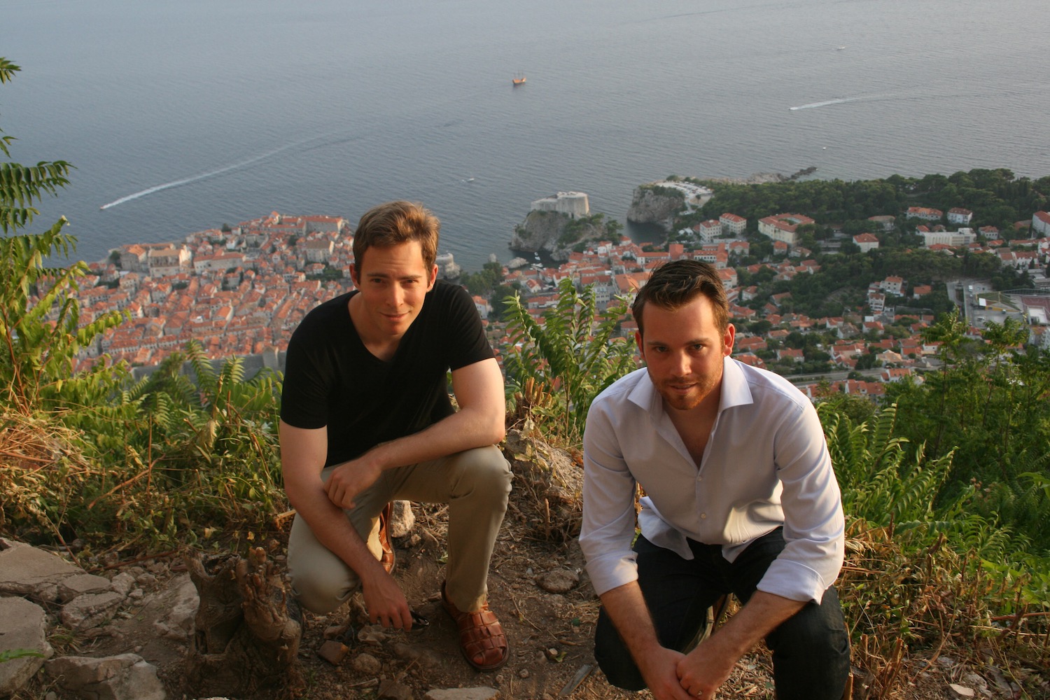 two men sitting on a hill with a city in the background