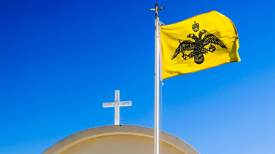 a yellow flag with a double headed eagle on a pole with a cross on top