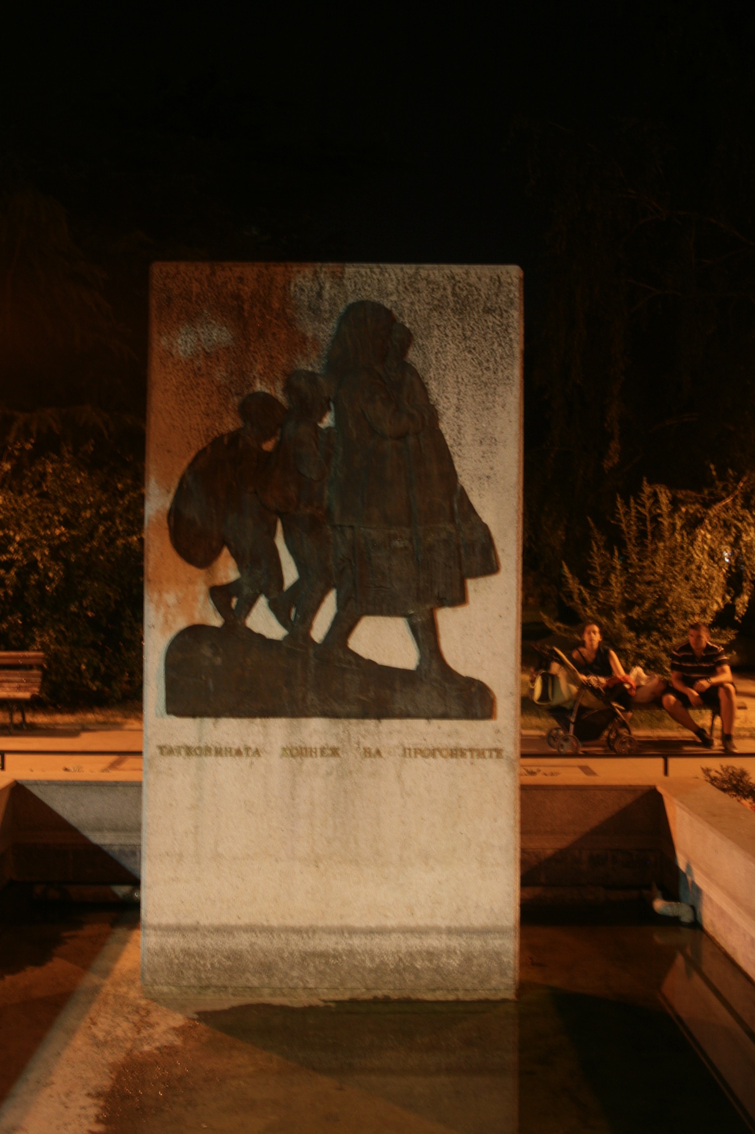 a stone statue with a picture of a group of people sitting on a bench