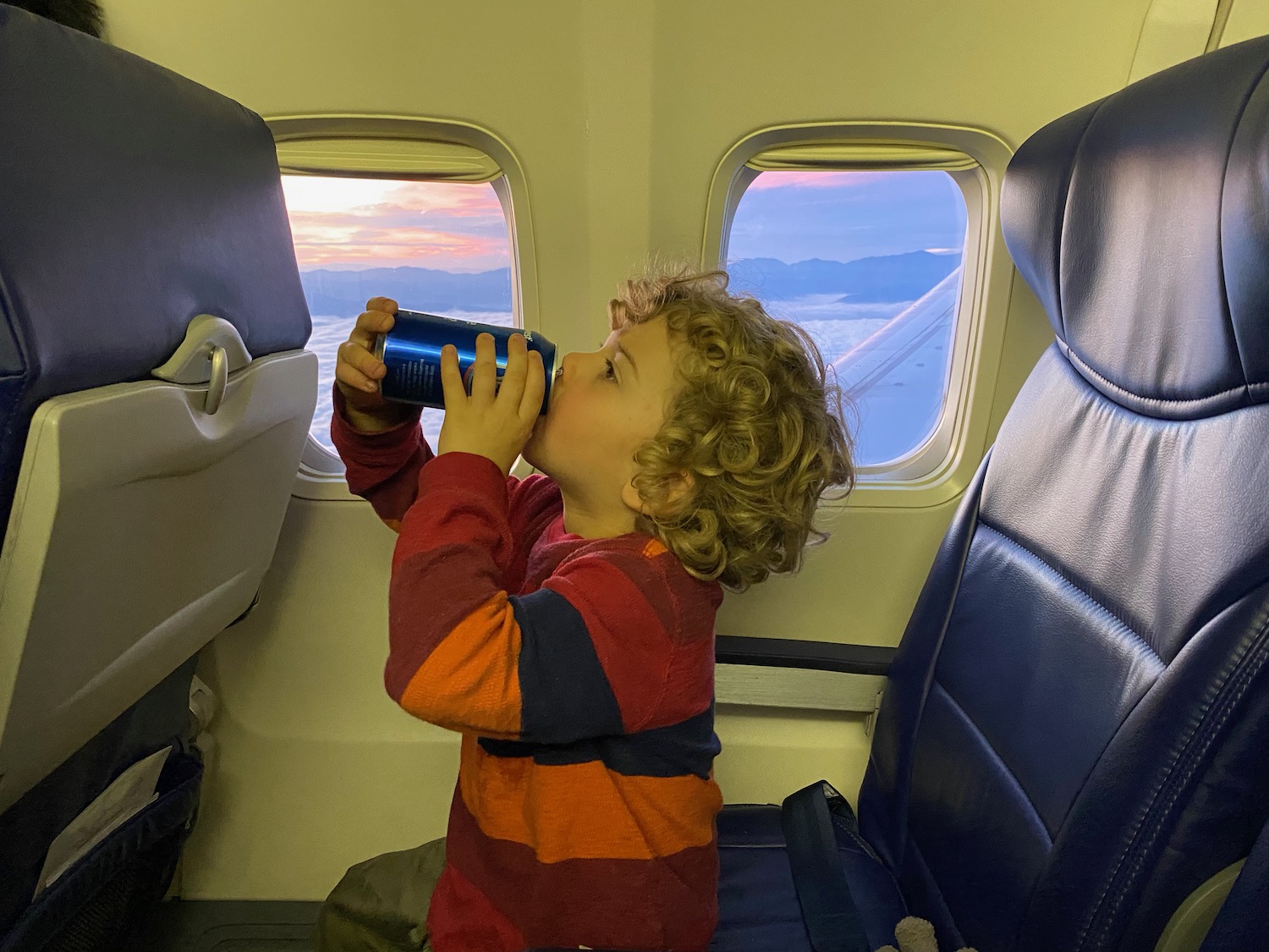 a child drinking from a blue can on an airplane