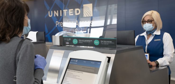 a group of people wearing face masks and standing at an airport check-in counter