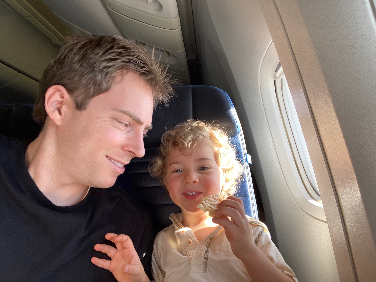 a man and child sitting in a plane eating popcorn