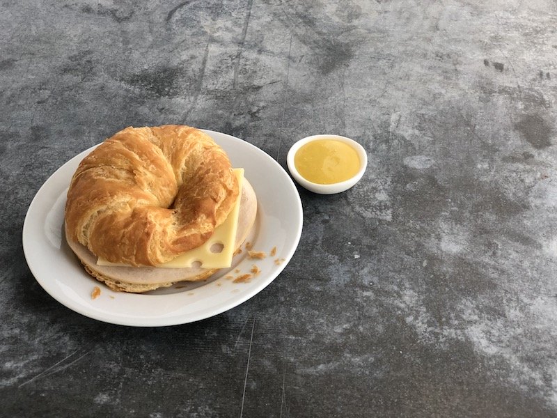 a croissant sandwich with cheese and a small bowl of mustard