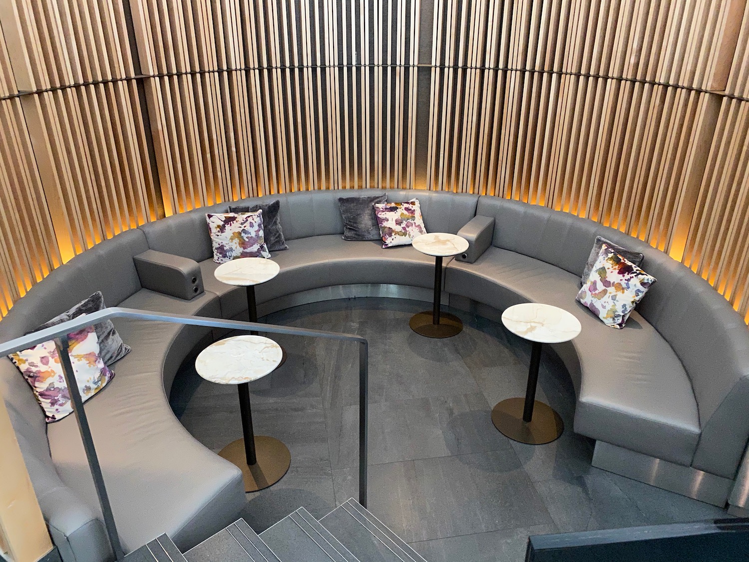 a round couch with tables and chairs in a room with wood slats