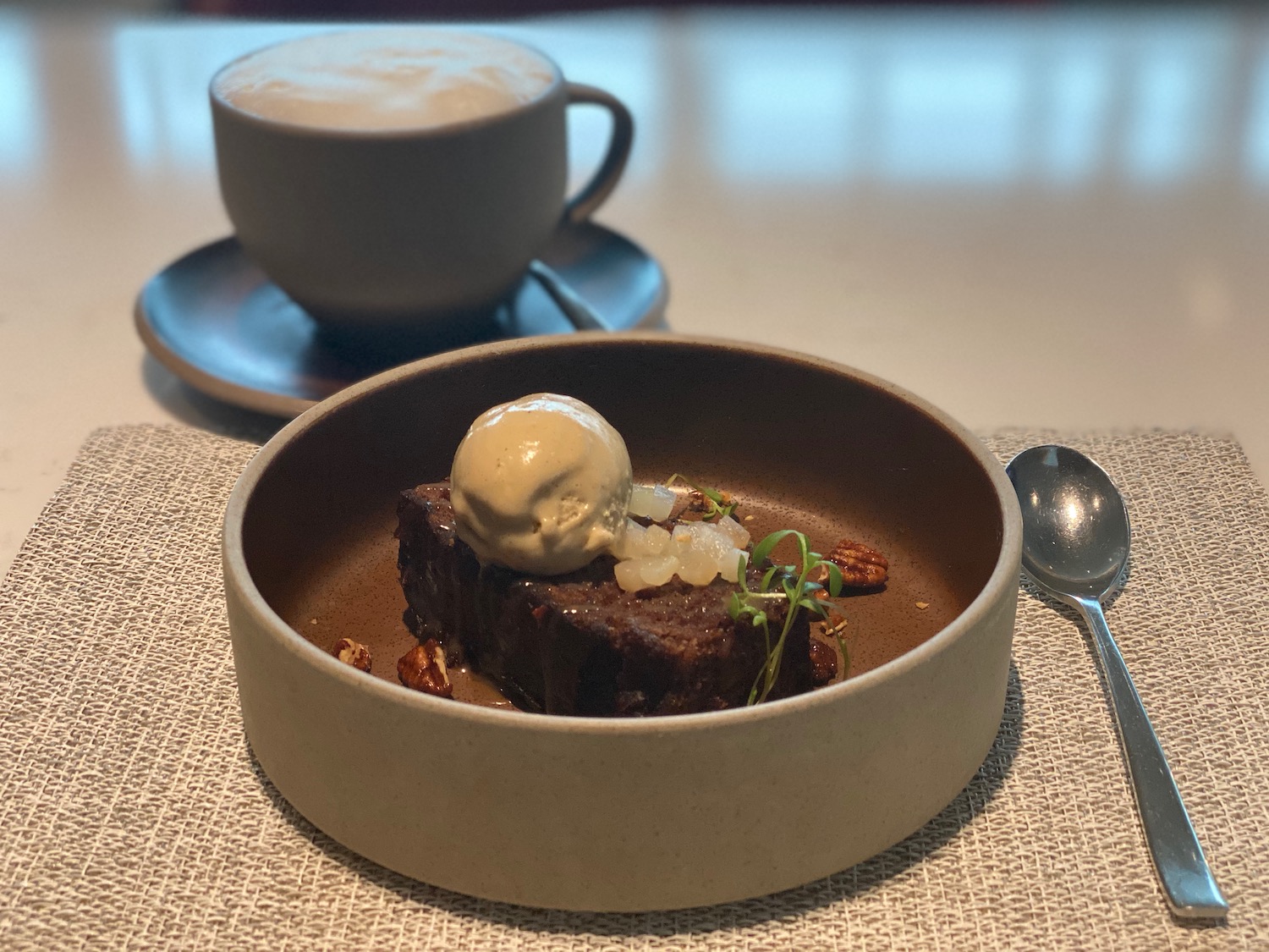 a brownie with ice cream in a bowl next to a cup of coffee