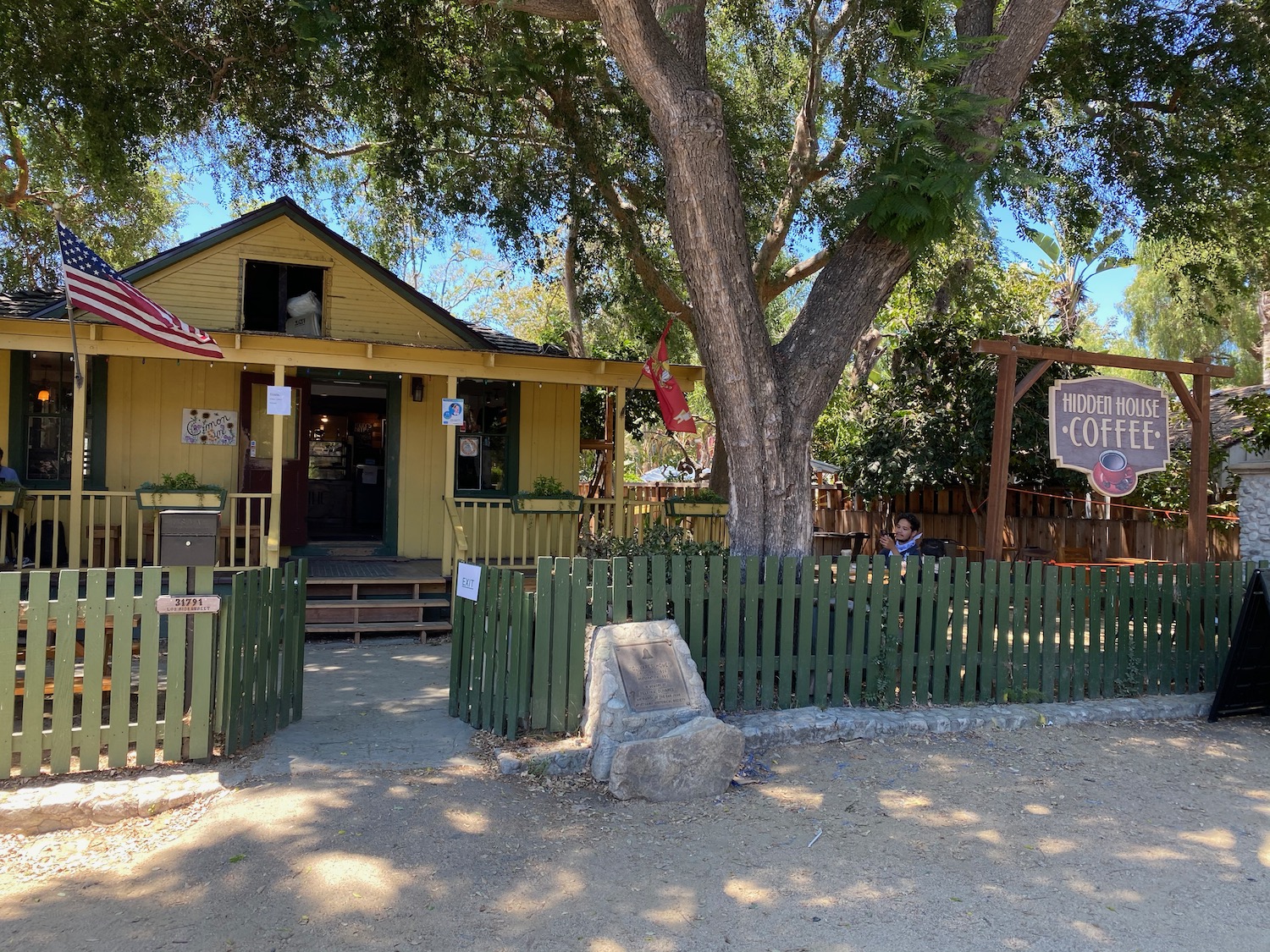 a small yellow house with a green fence and a tree