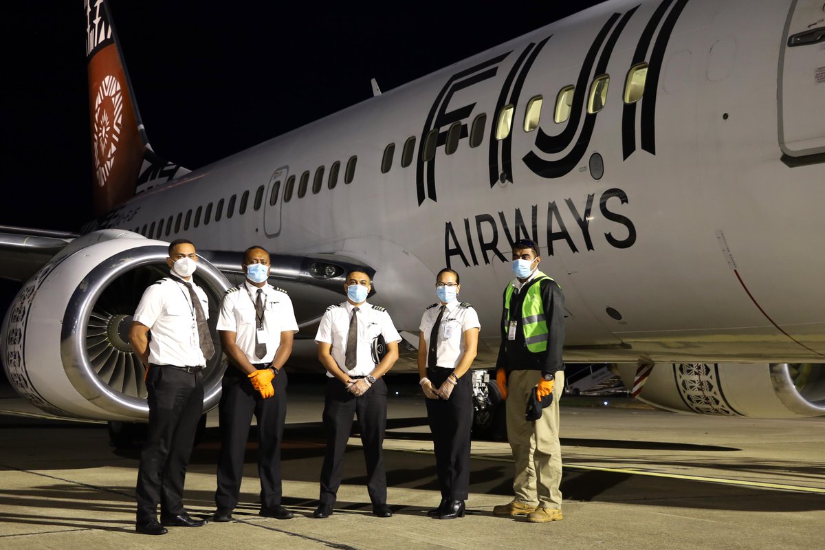 a group of people wearing face masks standing in front of an airplane