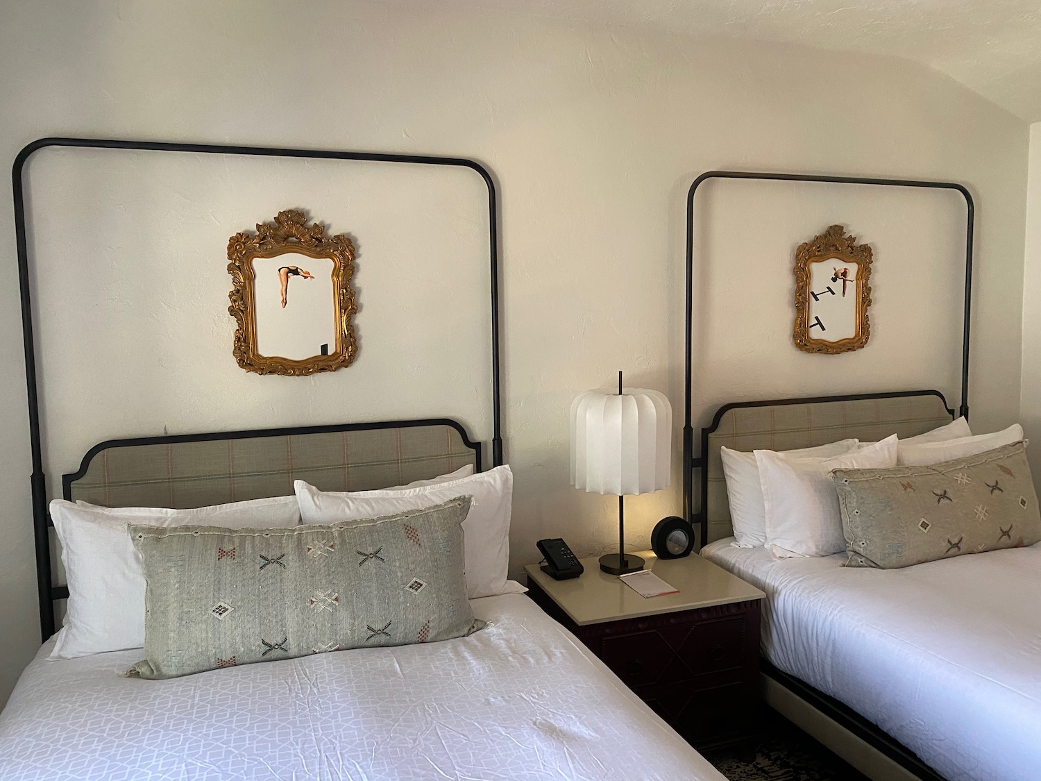 two beds with a lamp and a mirror above them