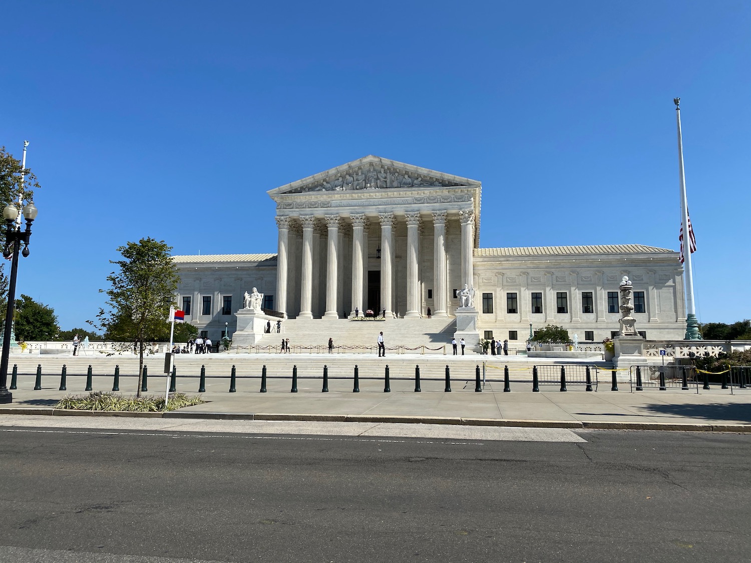 a white building with columns and a street and people walking with United States Supreme Court Building in the background