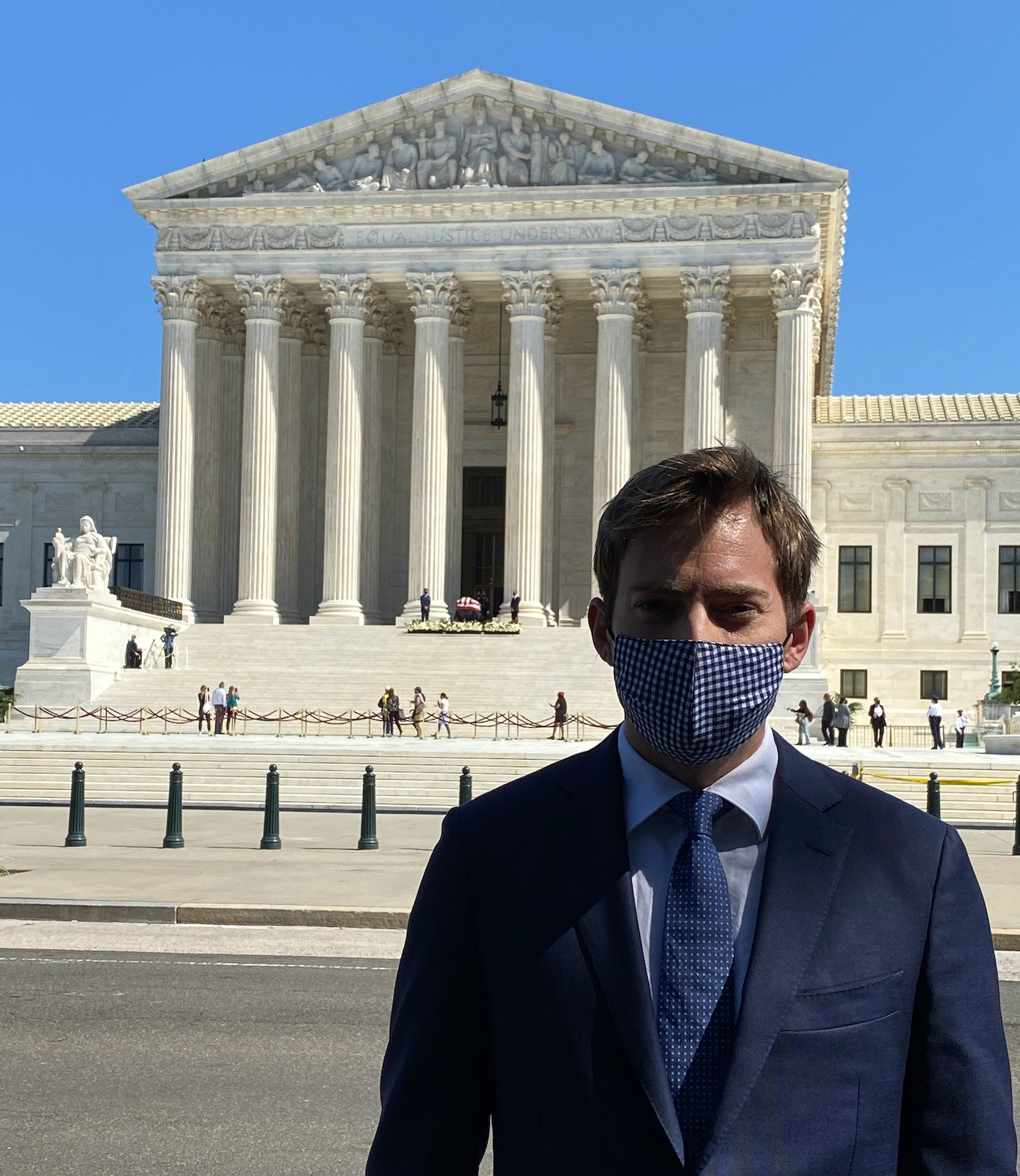 a man in a suit and tie wearing a mask in front of a white building with United States Supreme Court Building in the background