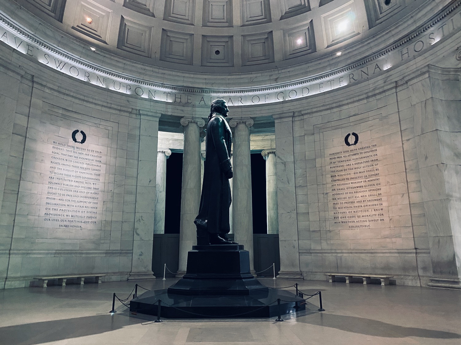 a statue in a room with columns and a wall with Jefferson Memorial in the background